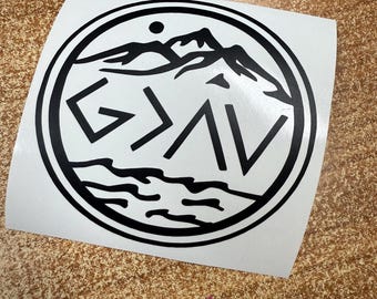 May include: A white sticker with a black circular design. The design features a mountain range, water, and the text "G > AV" in bold, stylized letters. A small dot is above the mountains.