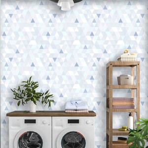 May include: A laundry room with a geometric wallpaper design in shades of white and blue. The room features a washing machine and dryer, a wooden shelf with towels and supplies, and a potted plant. Two laundry baskets are on the left.