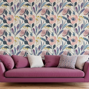 Puede incluir: Un sof&aacute; rosa con tres almohadas se encuentra frente a una pared con un patr&oacute;n de papel tapiz floral. El papel tapiz presenta flores rosas, hojas azules y moradas y un fondo crema.
