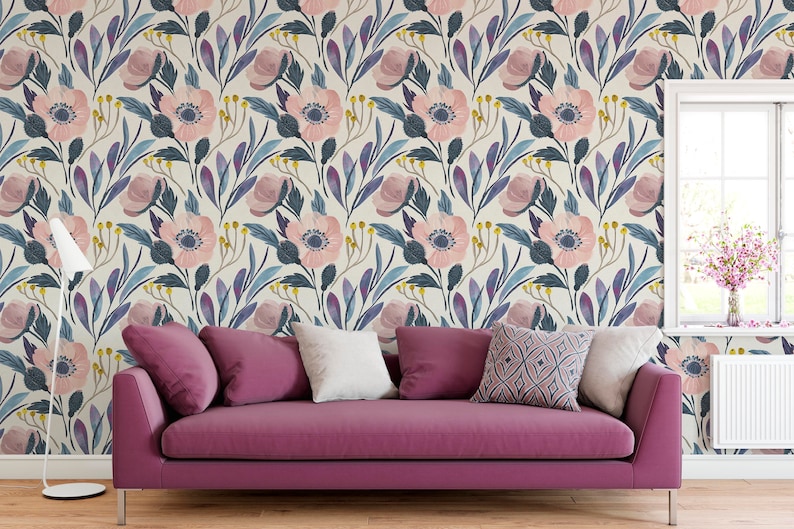 Puede incluir: Un sof&aacute; rosa con tres almohadas se encuentra frente a una pared con un patr&oacute;n de papel tapiz floral. El papel tapiz presenta flores rosas, hojas azules y moradas y un fondo crema.