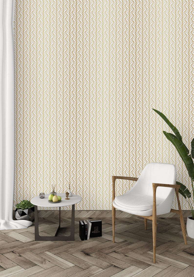 Puede incluir: Una silla blanca con patas de madera se encuentra frente a una pared blanca con un patr&oacute;n geom&eacute;trico dorado. Una peque&ntilde;a mesa redonda con una tapa blanca y patas negras se encuentra frente a la silla. La mesa tiene una peque&ntilde;a planta en maceta y un taz&oacute;n de fruta.