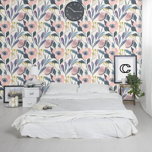 Puede incluir: Una cama blanca con un edred&oacute;n blanco y dos almohadas blancas se encuentra frente a una pared con un patr&oacute;n de papel tapiz floral. El papel tapiz presenta flores rosas y azules con hojas verdes sobre un fondo crema. Un reloj es visible en la pared.