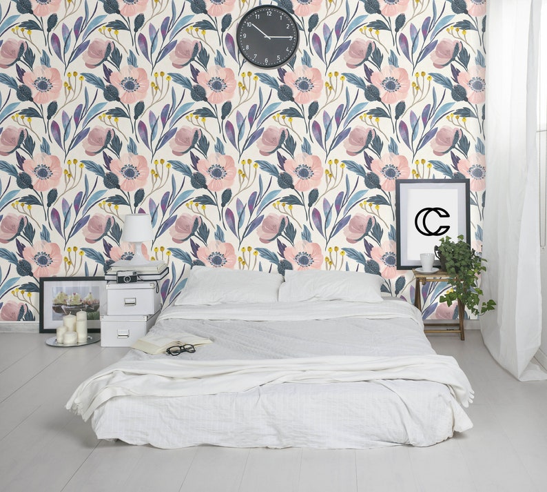 Puede incluir: Una cama blanca con un edred&oacute;n blanco y dos almohadas blancas se encuentra frente a una pared con un patr&oacute;n de papel tapiz floral. El papel tapiz presenta flores rosas y azules con hojas verdes sobre un fondo crema. Un reloj es visible en la pared.
