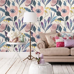 Puede incluir: Un interior de sala de estar con un sof&aacute; blanco, un suelo blanco y un puf blanco. La pared est&aacute; cubierta con un papel tapiz floral con flores rosas y hojas azules. Hay una l&aacute;mpara blanca con una pantalla blanca y una mesa auxiliar blanca con un jarr&oacute;n blanco y una figurita de p&aacute;jaro blanca.