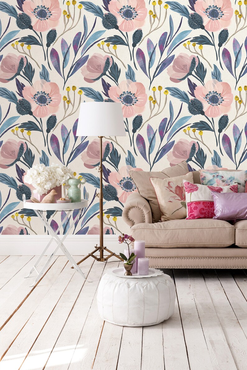 Puede incluir: Un interior de sala de estar con un sof&aacute; blanco, un suelo blanco y un puf blanco. La pared est&aacute; cubierta con un papel tapiz floral con flores rosas y hojas azules. Hay una l&aacute;mpara blanca con una pantalla blanca y una mesa auxiliar blanca con un jarr&oacute;n blanco y una figurita de p&aacute;jaro blanca.