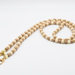 Könnte beinhalten: Ein Perlen-Lanyard mit abwechselnd hell- und dunkelbraunen Holzperlen. Das Lanyard hat goldfarbene Metallverschlüsse an jedem Ende. Die runden Perlen sind gleichmäßig angeordnet.