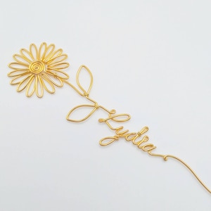 May include: Gold wire sculpture of a sunflower with a stem and leaves, with the name "Lydia" written in cursive below the flower.