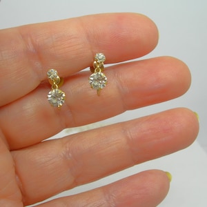 May include: A pair of gold dangle earrings with two clear round stones on each earring.