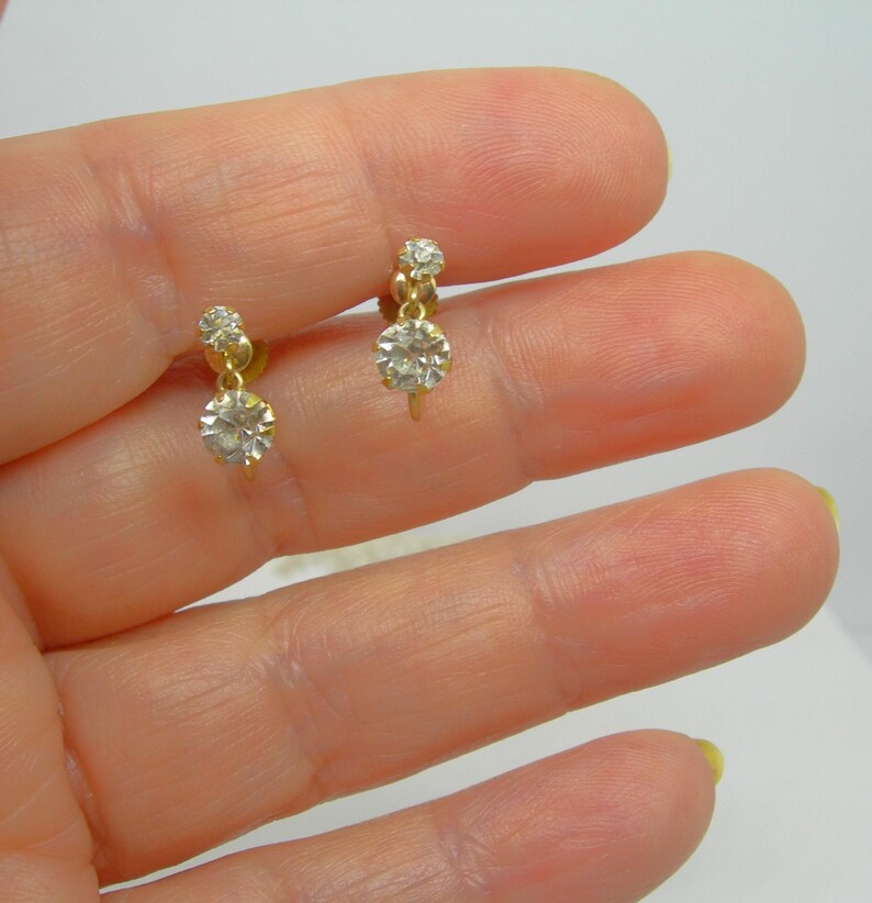 May include: A pair of gold dangle earrings with two clear round stones on each earring.