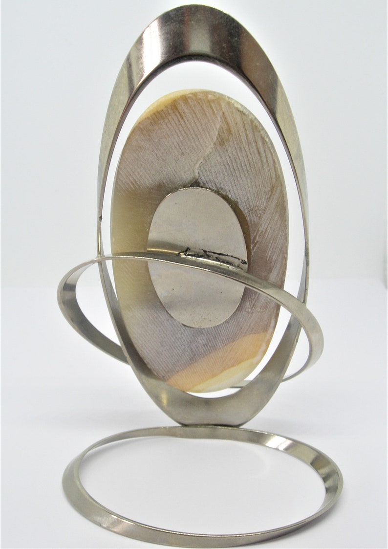 May include: A silver metal stand with a circular base and a curved, oval-shaped frame. A round, white and brown shell is displayed in the frame.