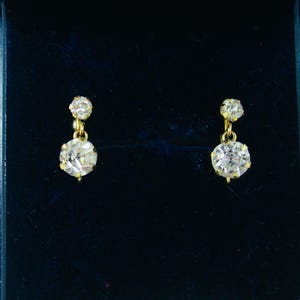 May include: A pair of gold earrings with two clear round stones on each earring.