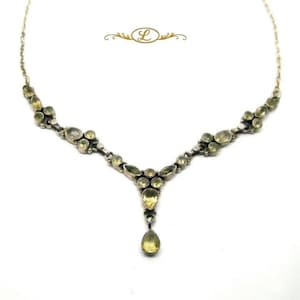 May include: A silver-toned necklace featuring a series of light yellow, oval and pear-shaped gemstones set in metal links. The centre of the necklace displays a prominent teardrop-shaped stone pendant. The letter L is centred above the jewellery.