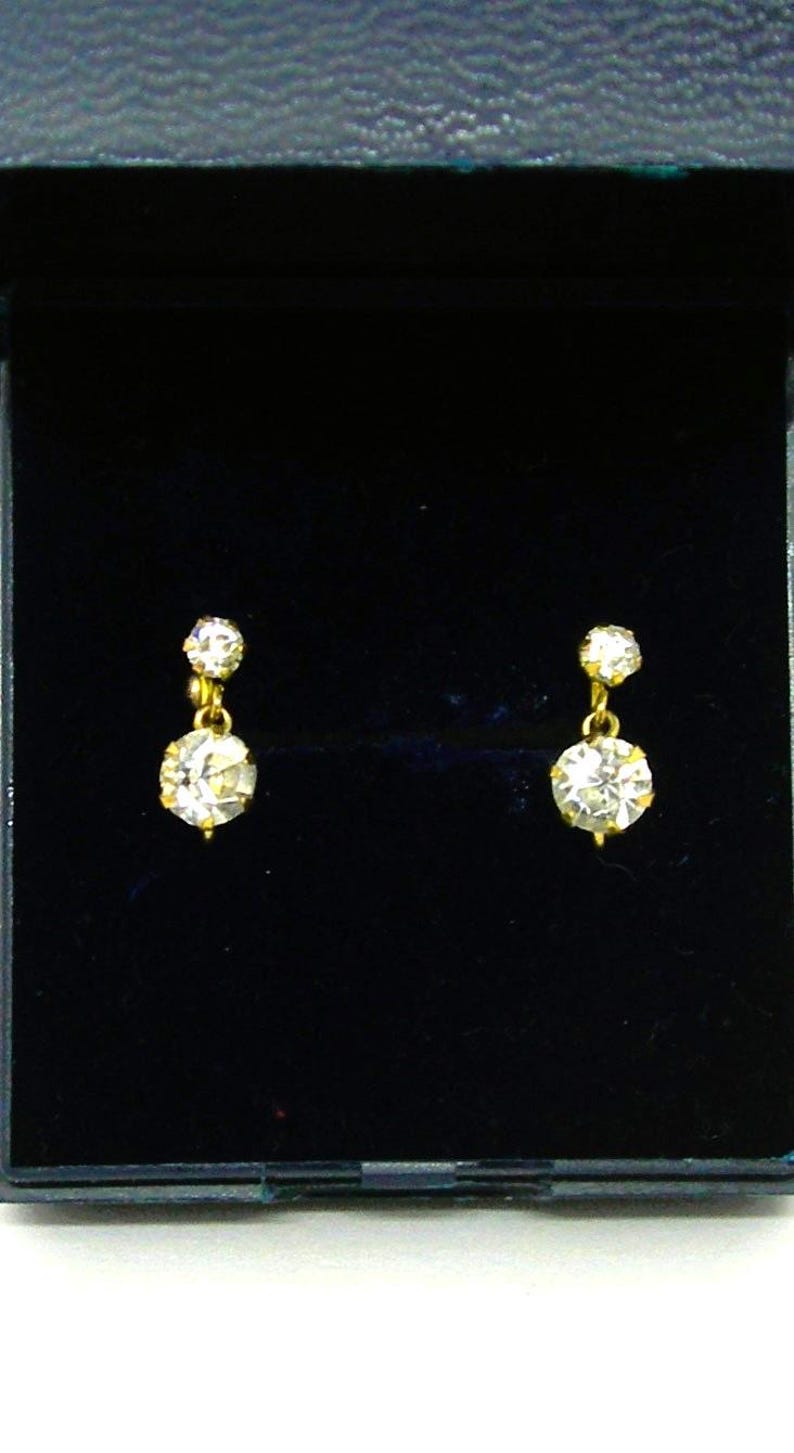May include: A pair of gold earrings with a single round clear stone on each earring.