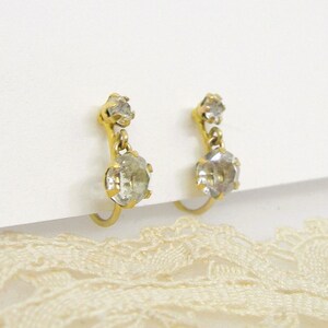May include: A pair of gold clip-on earrings with two clear crystal stones on each earring.