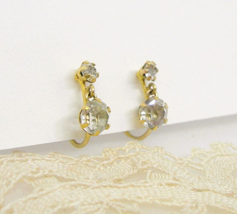 May include: A pair of gold clip-on earrings with two clear crystal stones on each earring.