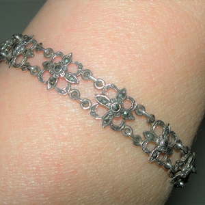 May include: A silver bracelet featuring a delicate chain and flower-shaped charms. Each charm is embellished with black marcasite stones.