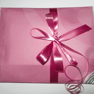 May include: A pink gift bag with a pink satin ribbon tied in a bow. The ribbon has a long tail that is curled.