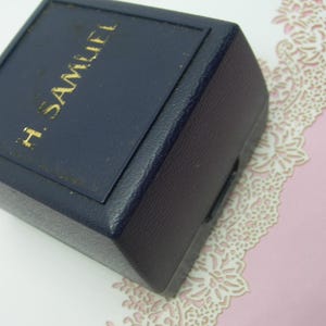 May include: A dark blue, square-shaped box with the text "H. SAMUEL" in gold lettering on the top.