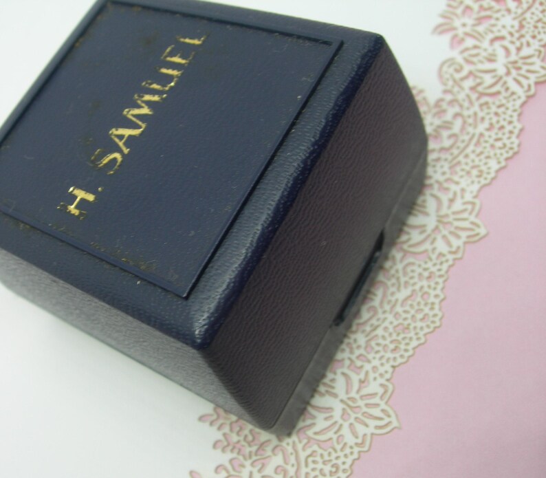 May include: A dark blue, square-shaped box with the text "H. SAMUEL" in gold lettering on the top.