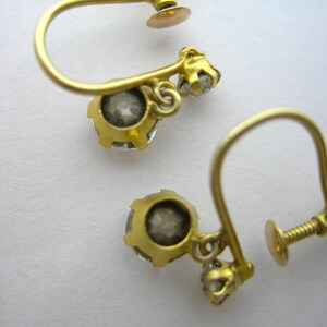 May include: A pair of gold earrings with a small clear stone on each earring. The earrings have a screw-back fastening.