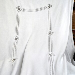 May include: A white textile featuring intricate openwork embroidery and cutwork details. The fabric displays a structured pattern of vertical bands connected by horizontal sections, accented with geometric diamond-shaped motifs throughout the design.