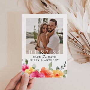 May include: Save the date card with a floral design featuring pink, yellow, and orange flowers. The card has a photo of a couple and the text "04.27.24 Save the Date Riley & Anthony".