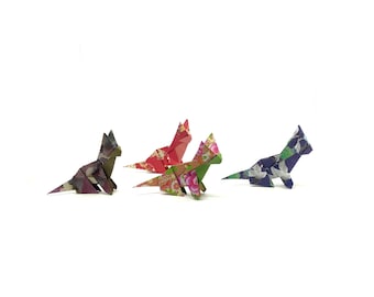 Może przedstawiać: Cztery figurki kota origami w różnych kolorach i wzorach kwiatowych ułożone na białym tle. Koty wykonane są z zagiętego papieru, z detalami takimi jak uszy i ogony. Kolory obejmują czerwony, zielony, fioletowy i brązowy.