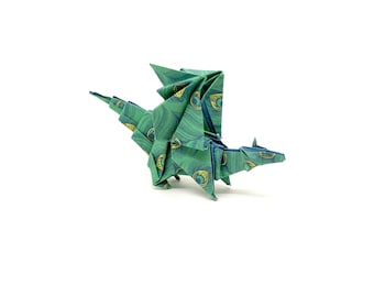 Może przedstawiać: Zielony smok origami z wzorami piór pawia. Papierowy smok ma rozłożone skrzydła i jest ustawiony na białym tle. Skrzydła, ciało i ogon smoka są szczegółowo zdobione powtarzającym się wzorem zieleni i złota.
