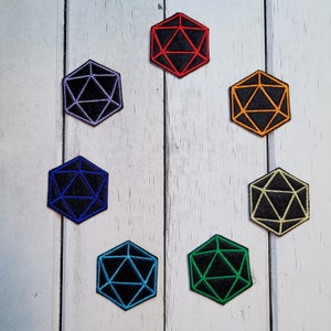 Peut inclure: Huit dés brodés en noir et blanc avec des contours de différentes couleurs. Les dés sont en forme de dé à 20 faces. Les contours sont rouge, orange, violet, bleu, vert et jaune.