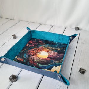 May include: A square collapsible dice tray with a teal exterior and a colorful interior print featuring a stylized sunset, dark trees, and swirling clouds. The tray corners are secured with silver-toned metal snaps, and it sits flat.