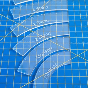 May include: A set of six clear plastic sewing rulers with curved edges. The rulers are labeled "5 Stand", "4 Stand", "3 Stand", "2 Stand", "Monster", and "Chariot".