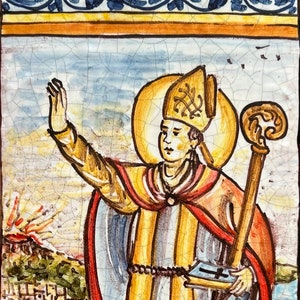 May include: A rectangular ceramic tile featuring a hand-painted illustration of Saint Gennaro wearing a miter and robes, holding a staff and book. The background depicts a volcano and coastal city. The text S. GENNARO is printed at the bottom.