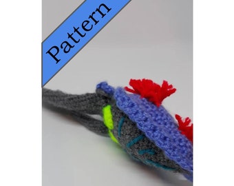 May include: A crocheted gray, blue, and green seahorse with red and white accents. The seahorse has a long tail and a small head with a pointed snout.
