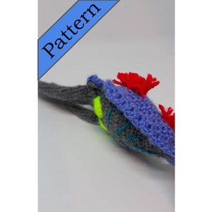May include: A crocheted gray, blue, and green seahorse with red and white accents. The seahorse has a long tail and a small head with a pointed snout.