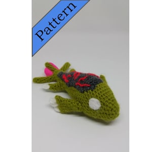 May include: A green crocheted lizard with a pink tail, black and red markings, and a white eye.