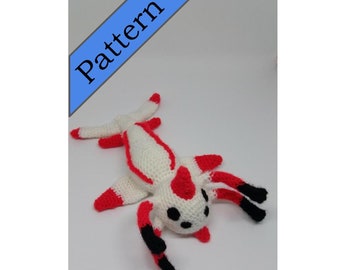 May include: White crocheted plush toy with red and black accents. The toy has a long body, four legs, and a head with black eyes.