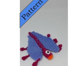 May include: A crocheted purple and pink dragon with orange and white eyes. The dragon has a long tail and four legs.
