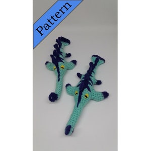 May include: Two crocheted seahorse toys, one larger than the other, are both teal blue with dark blue stripes and yellow eyes. The toys are posed on a white background.
