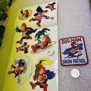 Puede incluir: Un conjunto de pegatinas vintage de Bud Man con un superhéroe de dibujos animados sosteniendo una cerveza. Las pegatinas están en una hoja de papel blanca con el texto "Bud Man" y "Bud's for you". También hay un parche de Bud Man con el texto "Bud Man Snow Patrol".