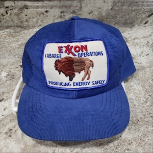 Puede incluir: Gorra de béisbol de pana azul con un parche blanco que muestra un búfalo marrón y blanco y el texto "Exxon Operations, Barge Producing Energy Safely".