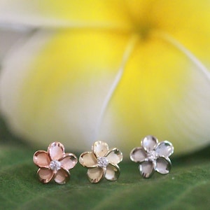 May include: Three flower-shaped earrings with a single diamond in the center of each. The earrings are in rose gold, yellow gold, and silver.