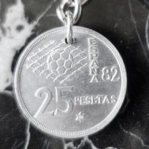 May include: Silver keychain featuring a 25 pesetas coin from Spain 1982 with a football in a net design. The coin has the text "ESPAÑA 82" and "25 PESETAS".