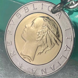 May include: A silver and gold coin keychain. The coin displays a profile and the words "REPUBBLICA ITALIANA". The keychain has a silver chain and a silver ring.