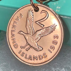 May include: A copper-coloured keychain featuring a Falkland Islands coin from 1983. The coin shows a goose in flight and the number 2. The keychain has a rose gold-coloured ring and chain.