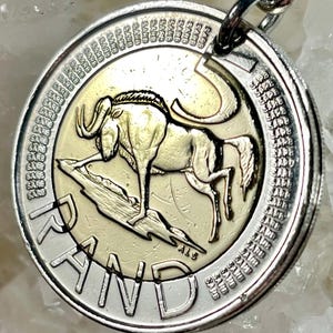 Könnte beinhalten: Eine südafrikanische 5-Rand-Münze aus Silber mit einem Gnu auf einem felsigen Ausläufer. Die Münze trägt die Inschriften "RAND" und "SARB" am Rand.