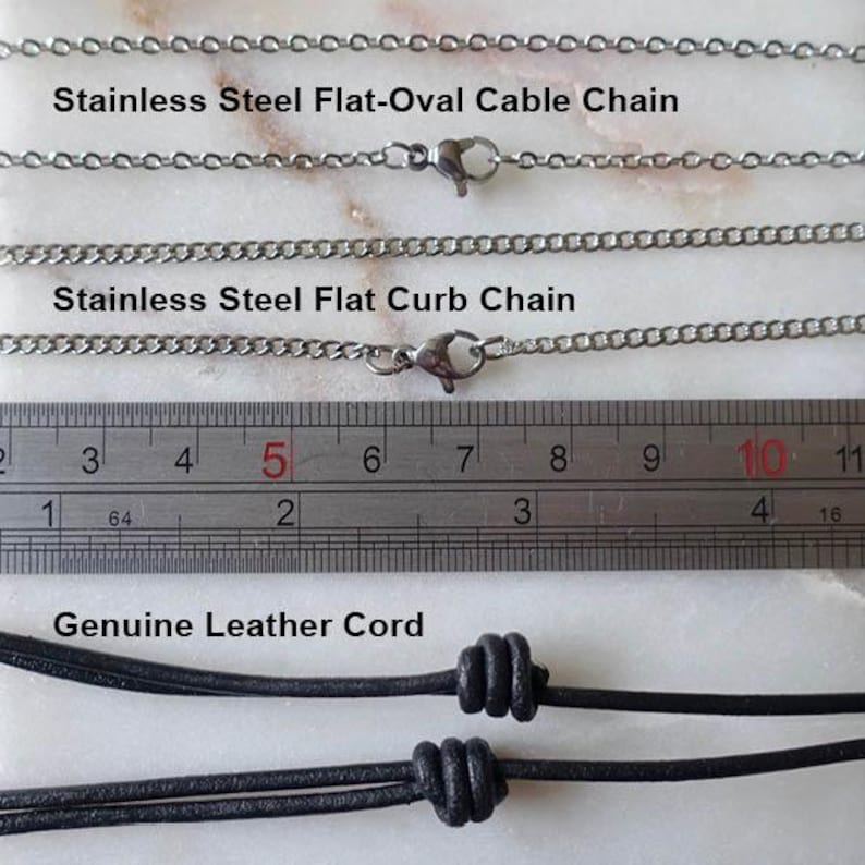 Puede incluir: Primer plano de tres estilos de cadenas de collar: cadena plana ovalada de acero inoxidable, cadena plana de eslabones de acero inoxidable y cord&oacute;n de cuero genuino. Una regla muestra las medidas en cent&iacute;metros. Texto que etiqueta cada tipo de cadena.
