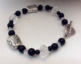 May include: A beaded bracelet featuring black onyx beads, clear crystal accents, and two silver-toned, textured focal beads. The bracelet is secured with a decorative toggle clasp.