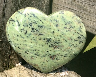 May include: A green heart-shaped stone with black and brown speckles.