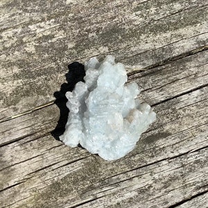 Pu&ograve; includere: Un gruppo di cristalli di celestite blu chiaro su una superficie di legno invecchiato.