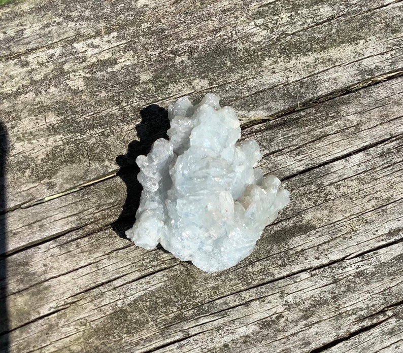 Pu&ograve; includere: Un gruppo di cristalli di celestite blu chiaro su una superficie di legno invecchiato.